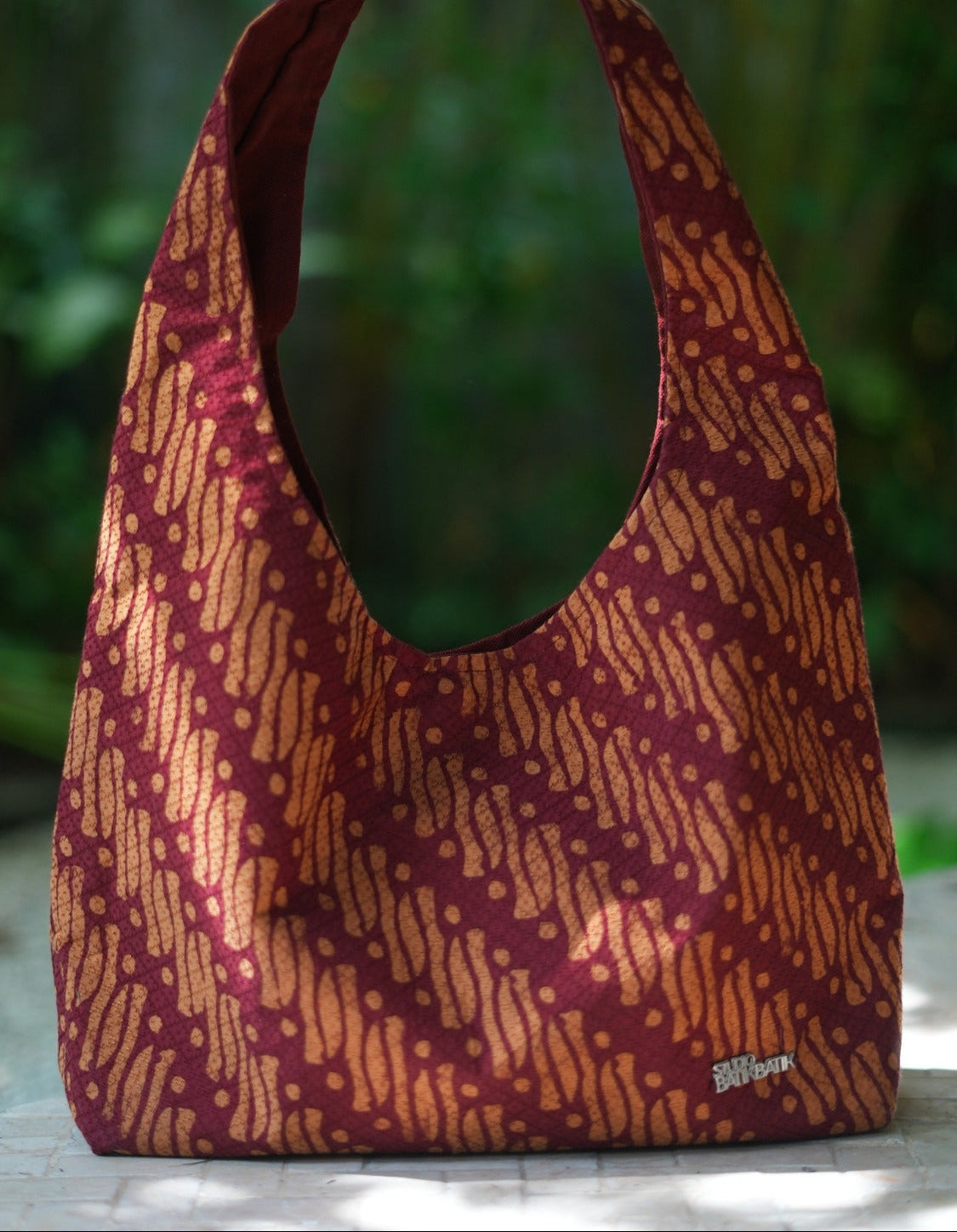 Brown batik patternd with parang motif red and orange. patterned handbag on a wooden surface with a blurred green background