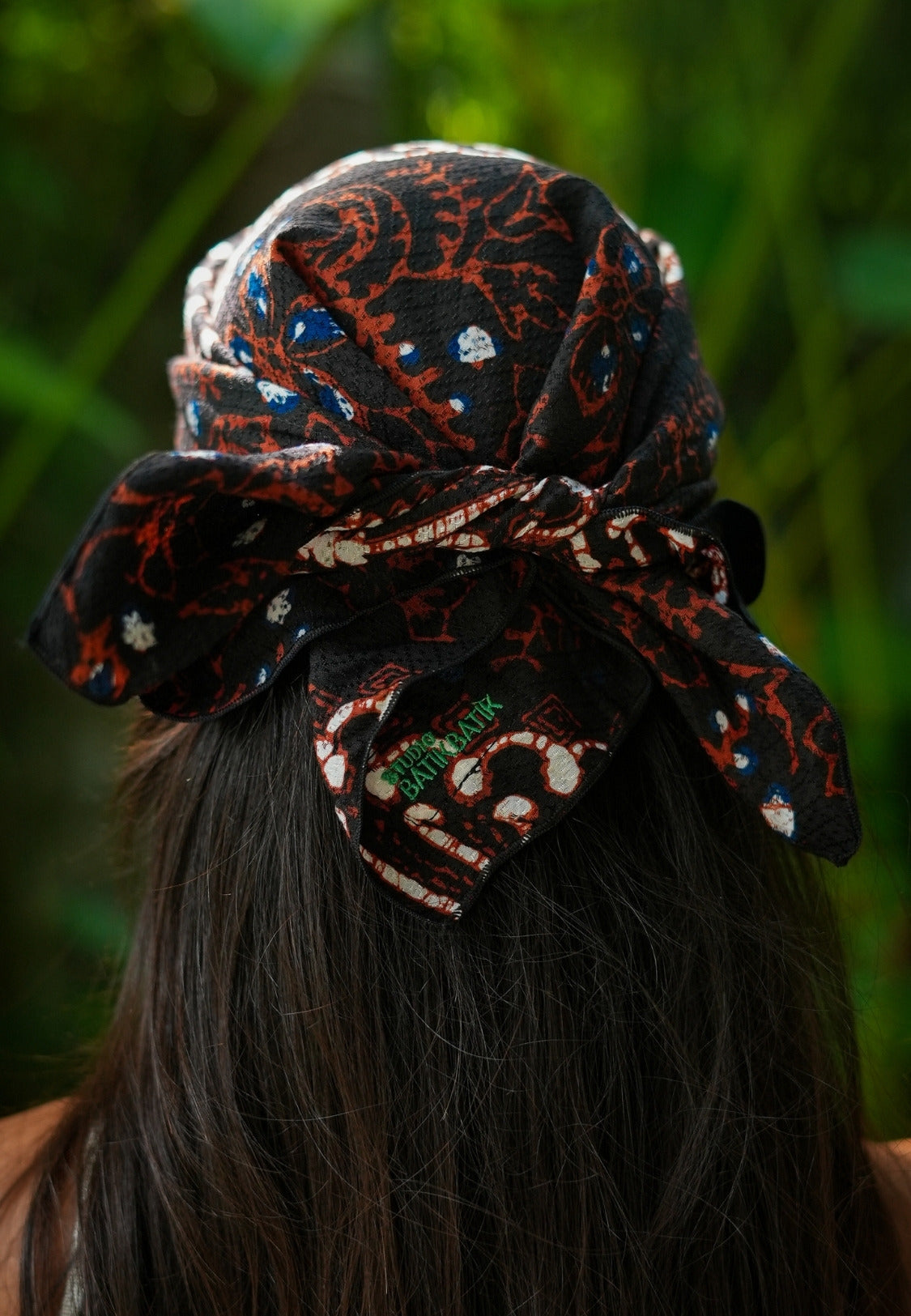 Person wearing a batik parang patterned headscarf with a blurred green background