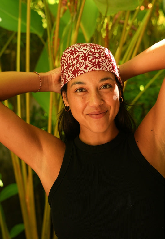 Woman wearing a red batik headscarf with green foliage in the background
