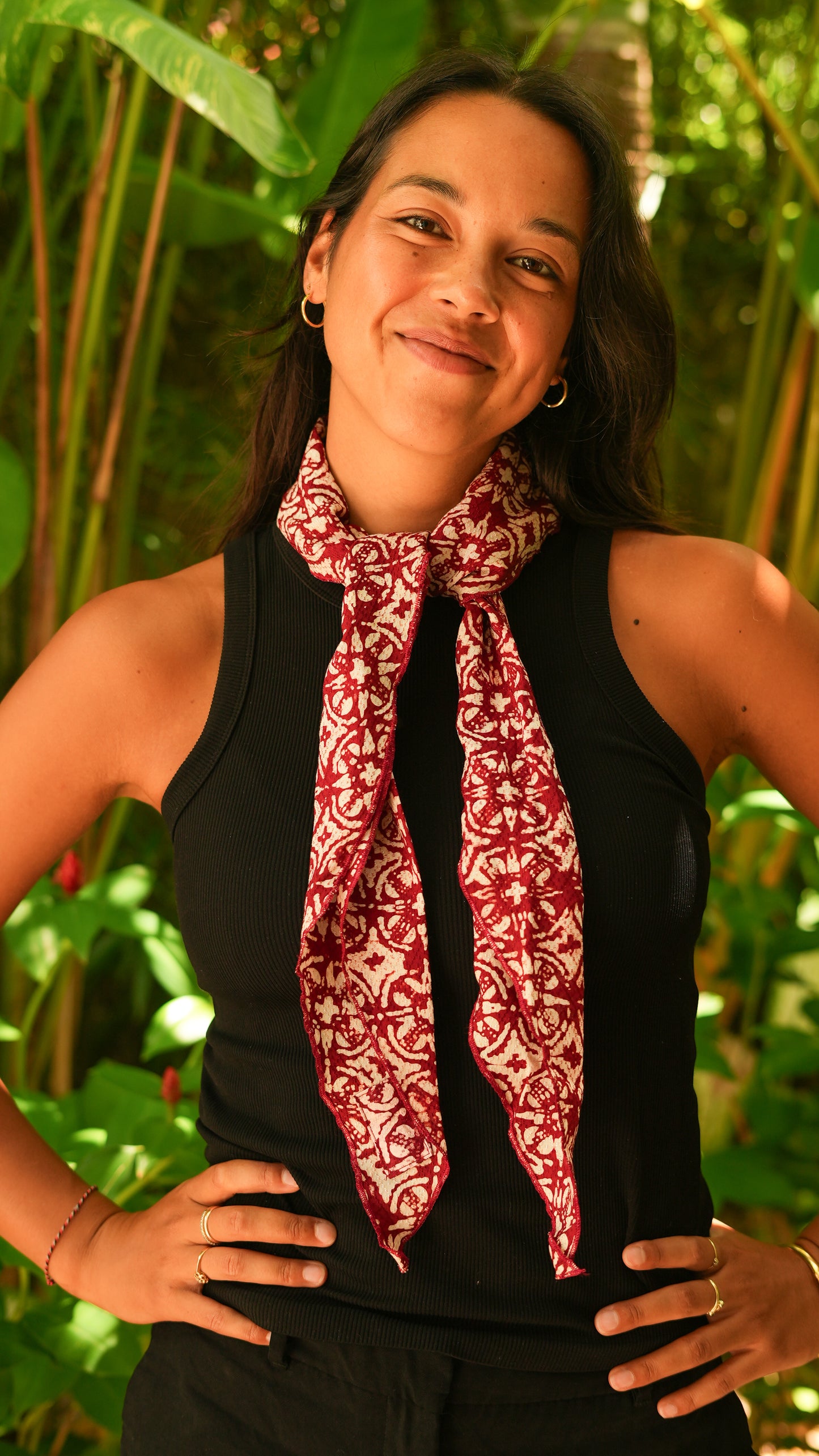 Woman wearing a red batik scarf in front of green foliage