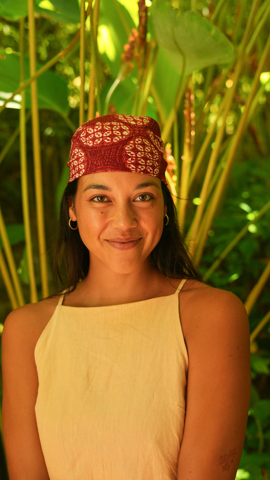 Woman wearing a red batik headscarf with white patterns against a green leafy background