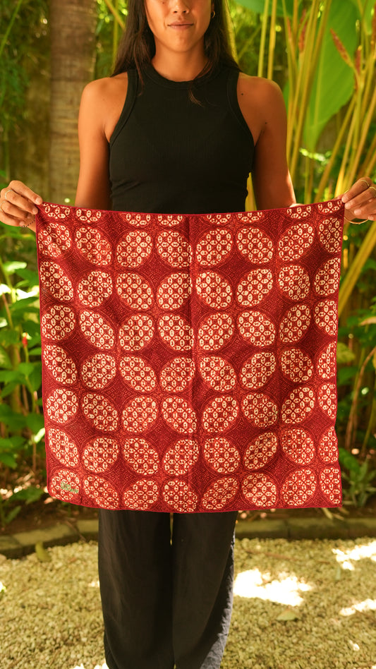 Person holding a red patterned batik fabric against a natural background
