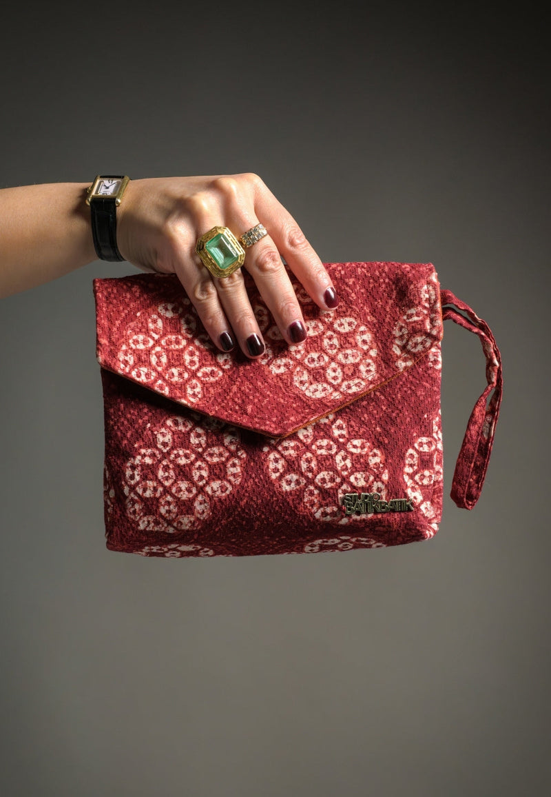Red patterned Batik clutch held by a hand against a gray background