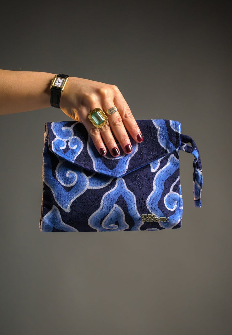 Hand holding a blue patterned Batik clutch against a gray background