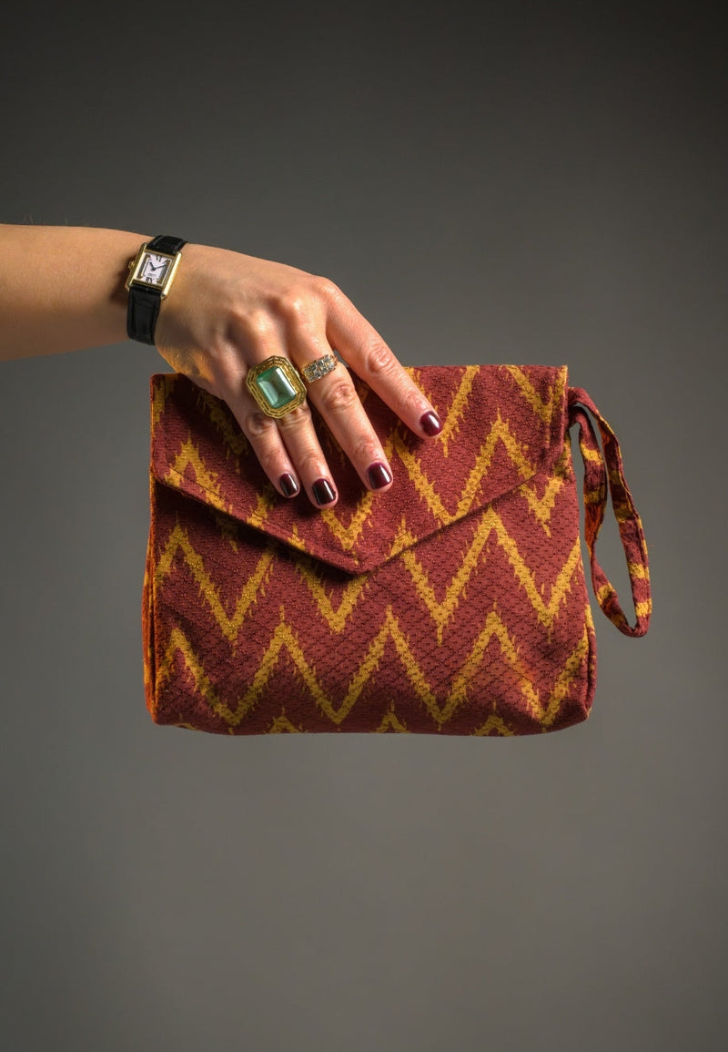Hand holding a red and yellow zigzag patterned Batik clutch against a gray background