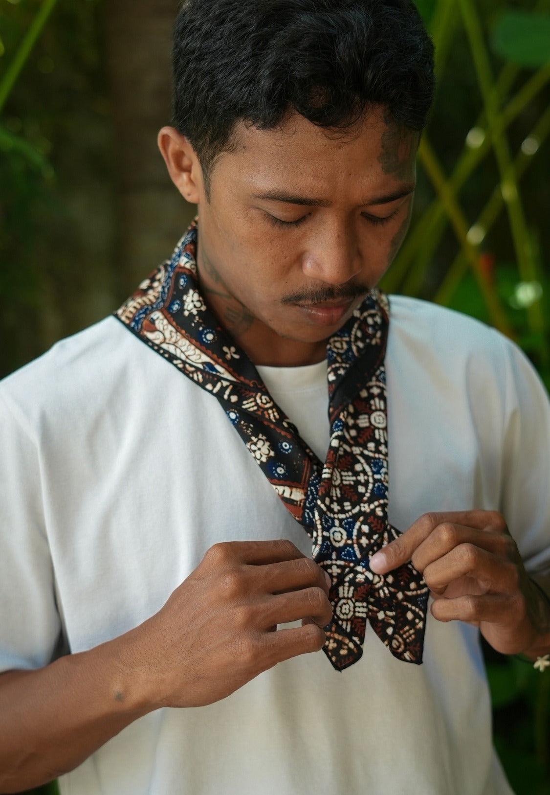 Man adjusting a patterned bow tie outdoors with a batik pattern nitik