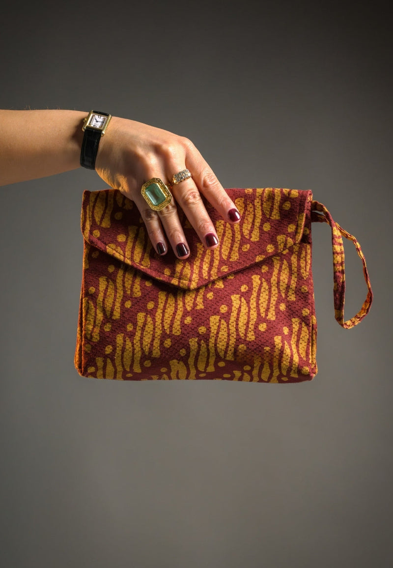 Hand holding a patterned Batik clutch bag against a gray background