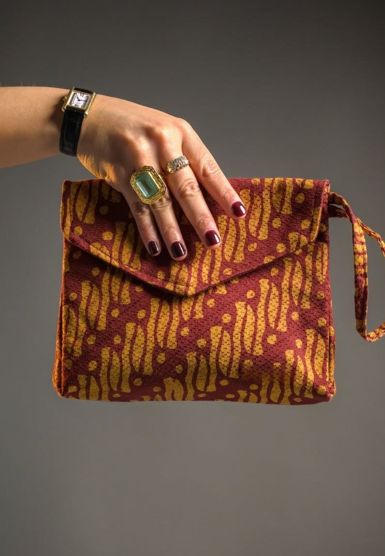 Hand holding a patterned batik parang clutch bag against a gray background