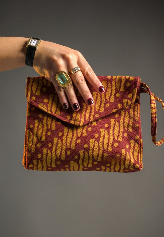 Hand holding a patterned batik parang clutch bag against a gray background
