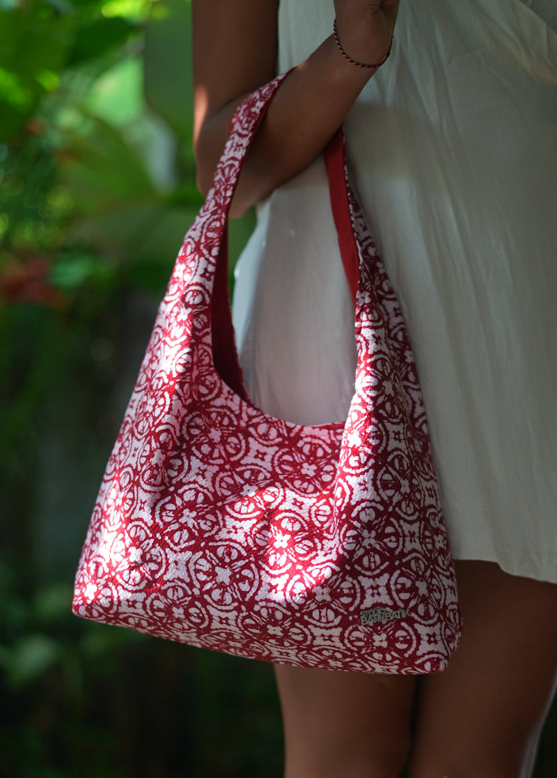 Red and white Batik patterned triangle-shaped pouch held by a person with a blurred natural background