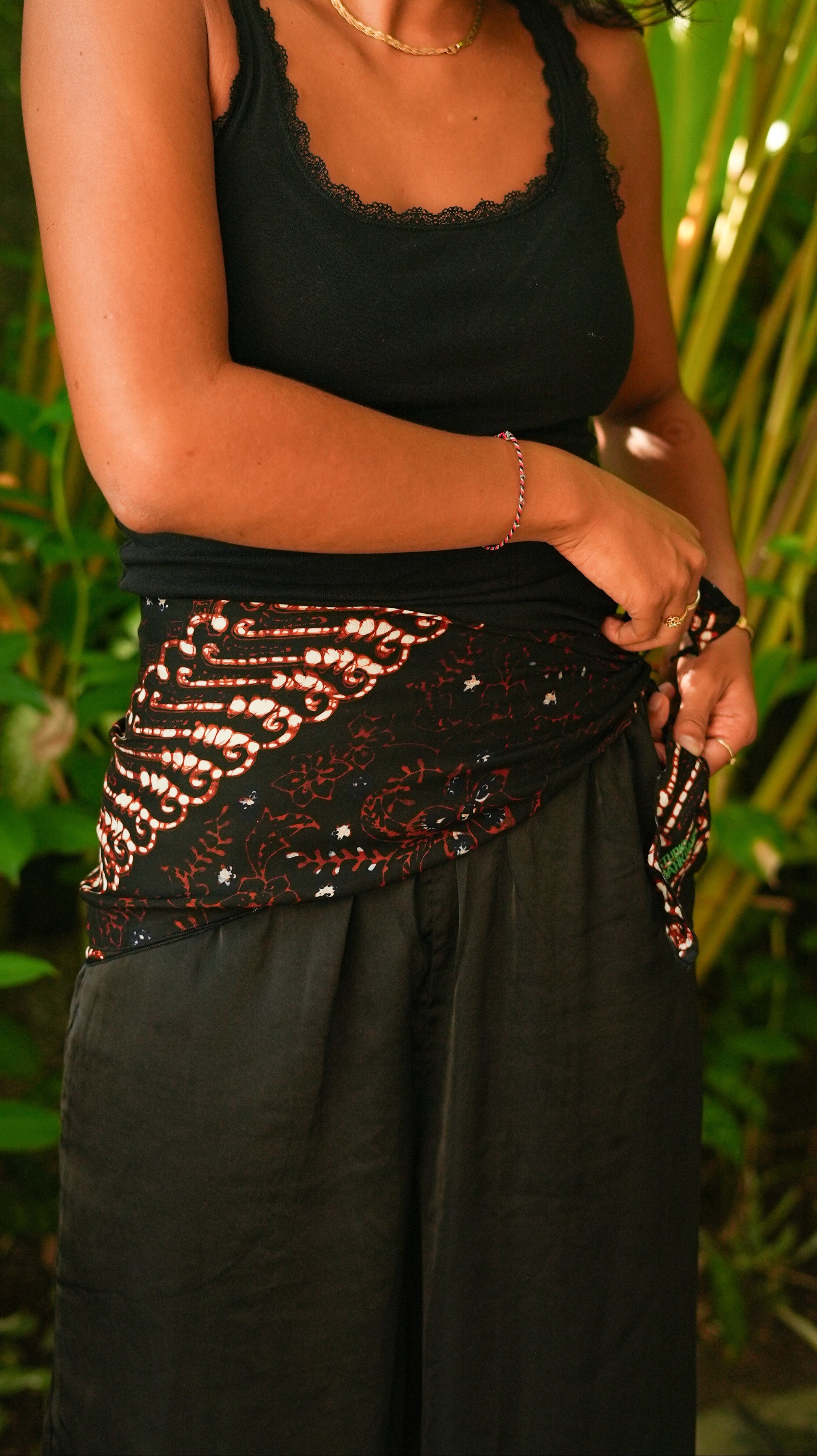 Person wearing a black top with decorative waistband against a natural background