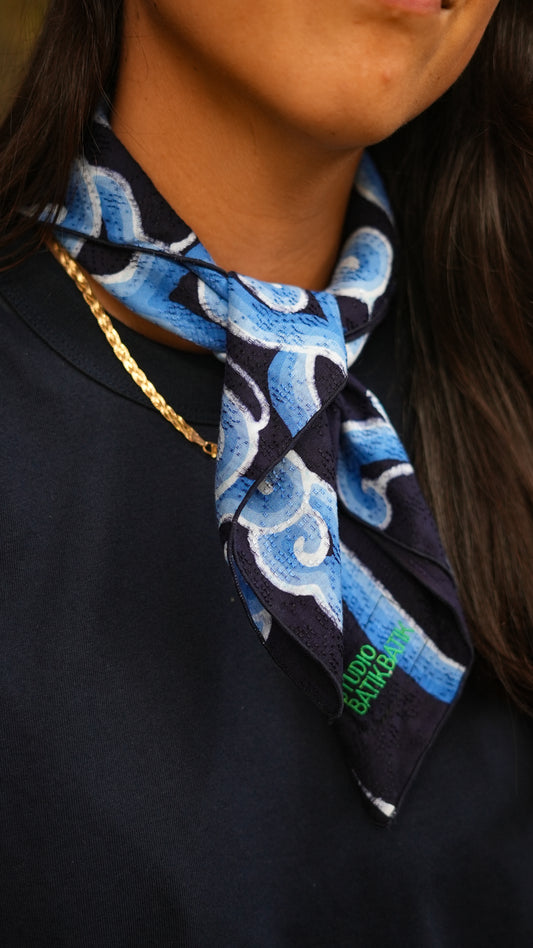 Person wearing a blue batik patterned scarf with a brand logo on a dark background