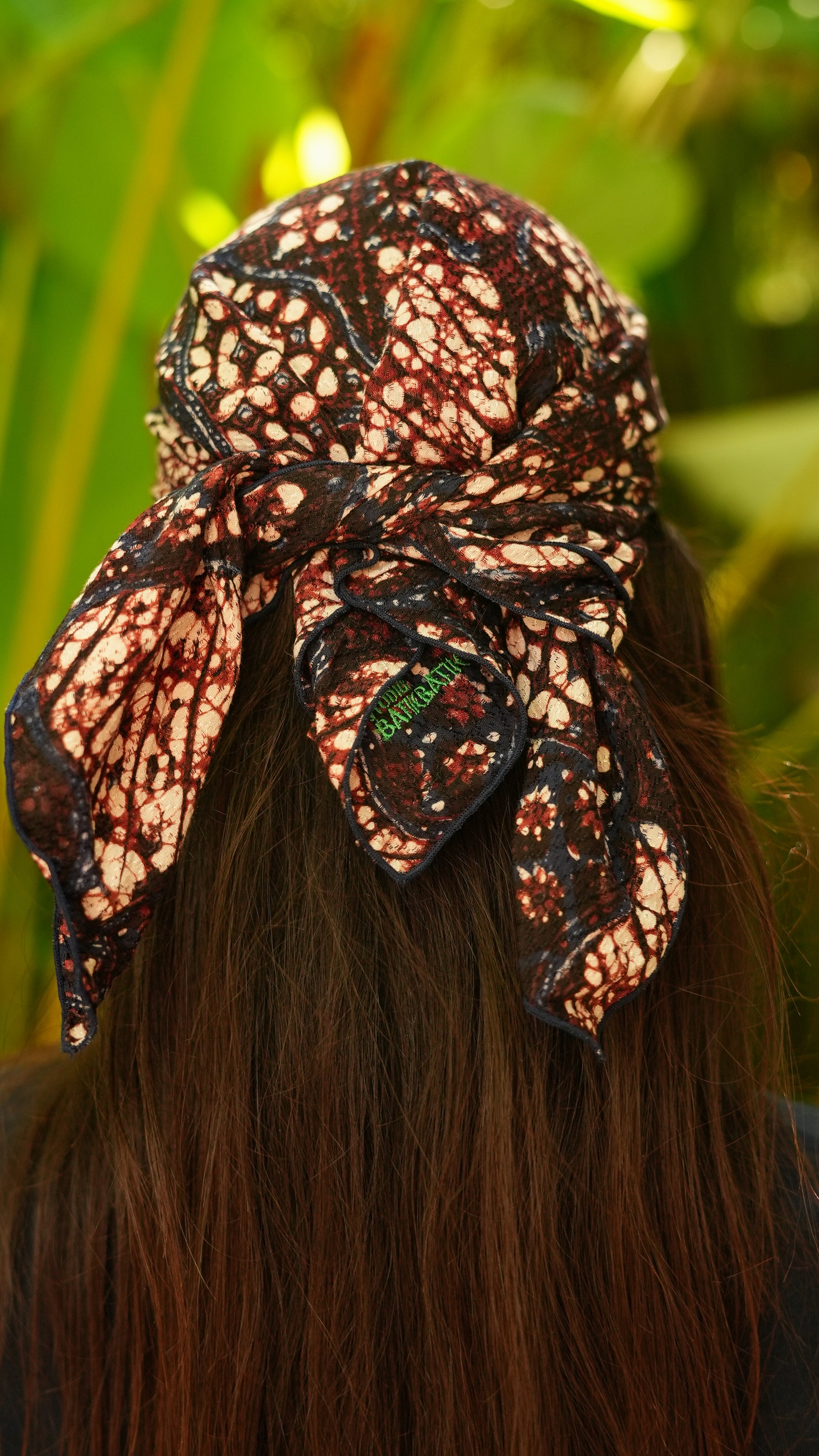 Person wearing a batik headscarf with intricate patterns and a green leaf detail.