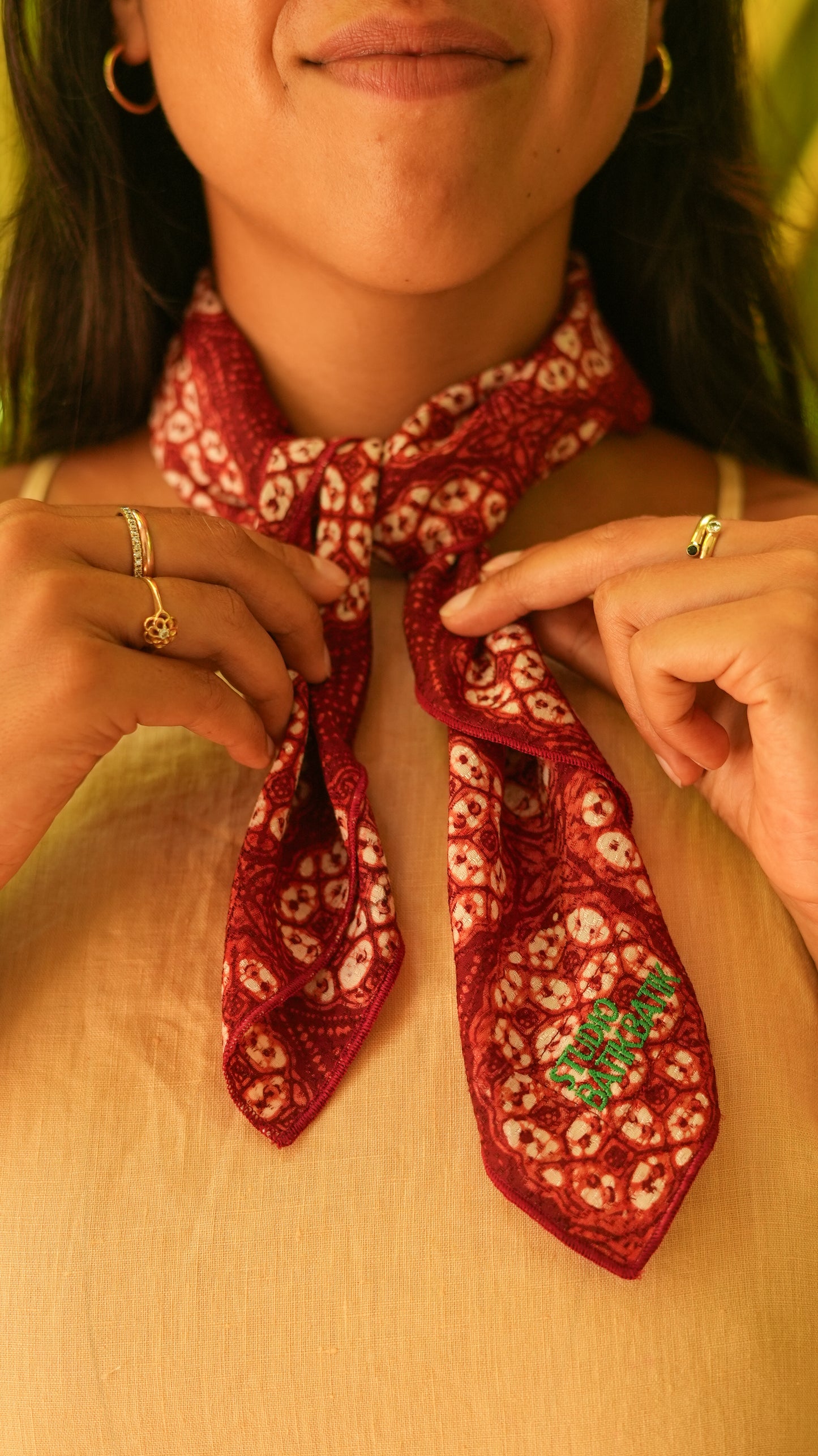 Person wearing a red patterned batik scarf around their neck with a blurred background