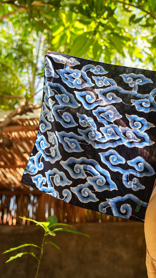 Black fabric with blue batik patterns held by a person against a natural background