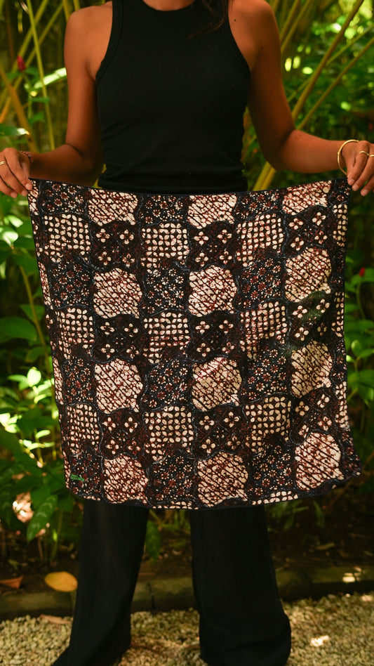 Person wearing a batik patterned skirt with a black top and pants against a natural background