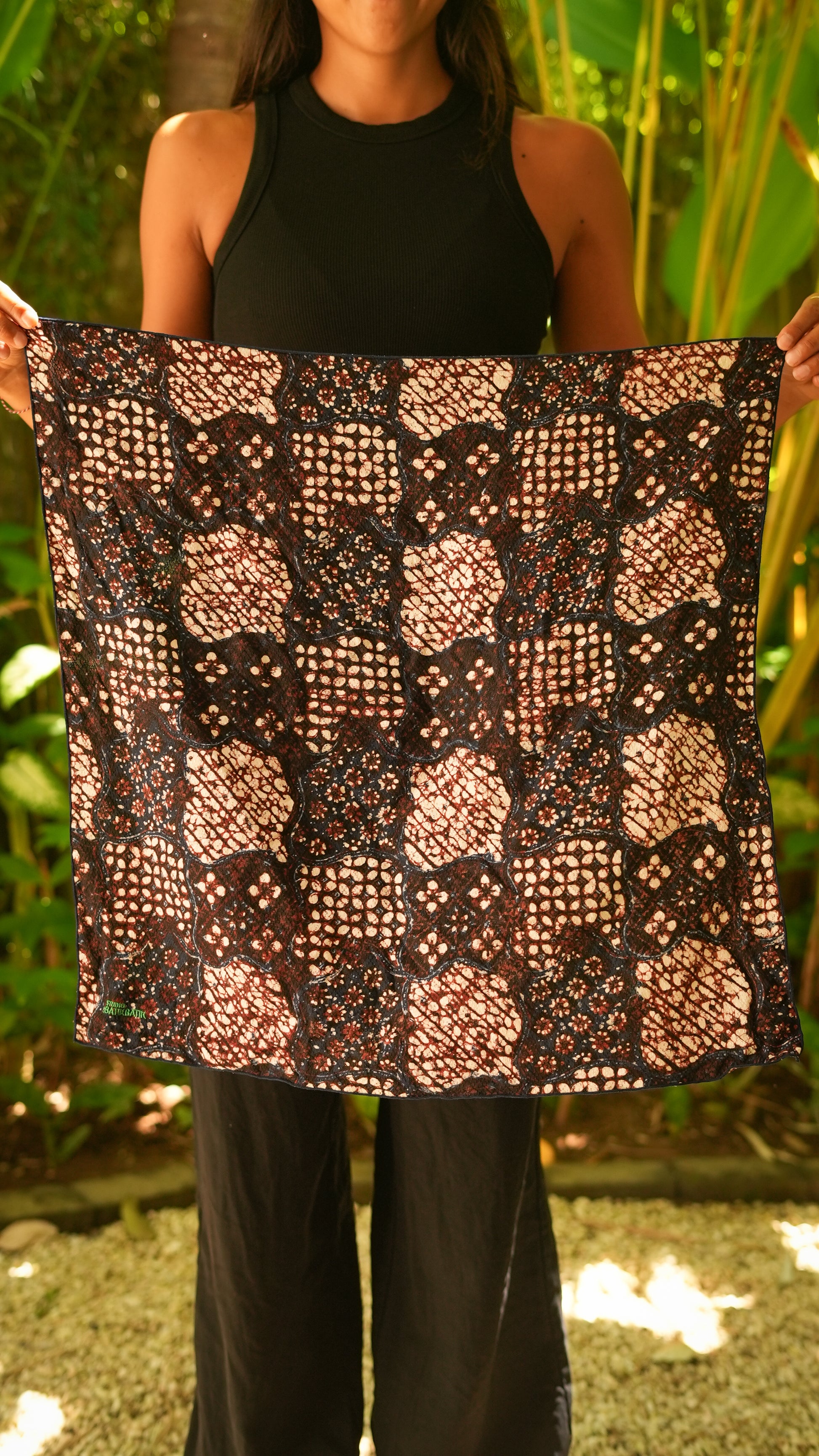 Person holding a patterned batik fabric in front of a natural background