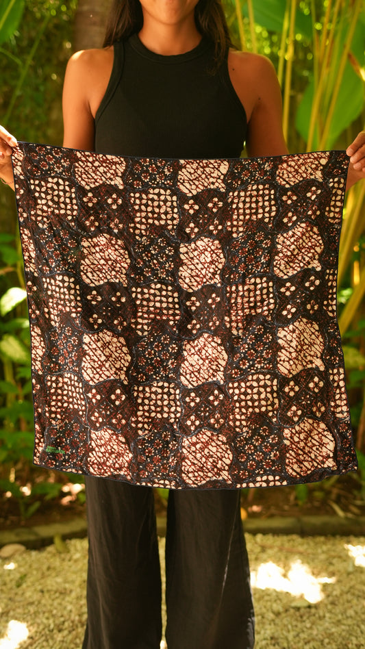 Person holding a patterned batik fabric in front of a natural background