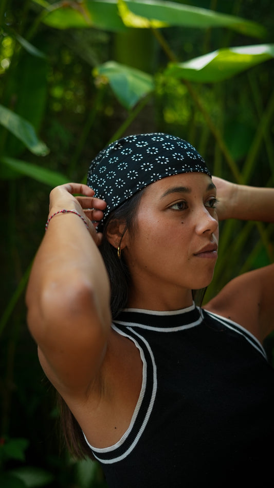 Woman adjusting a headband against a green leafy background. Girl wearing a Batik bandana on her head with whte and black colors batik titik