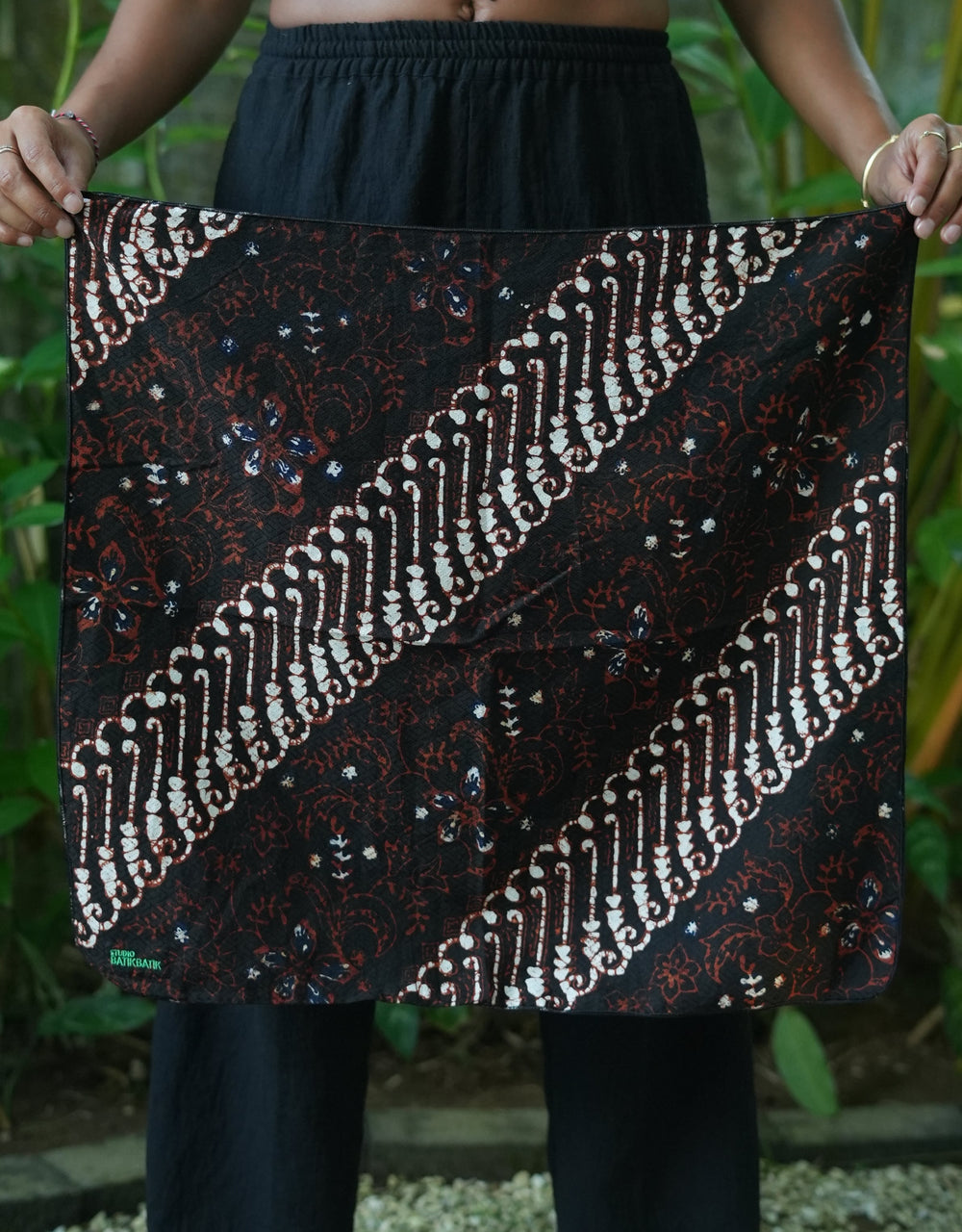 Person holding a brown batik bandana fabric with intricate patterns outdoors