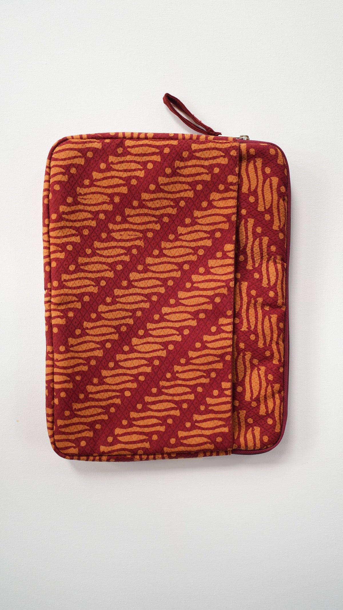 A zippered batik laptop sleeve or pouch with a red and orange batik-style pattern, shown flat against a plain white background.