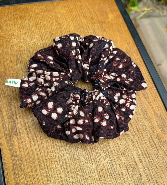 Black and white patterned scrunchie on a wooden surface with greenery in the background