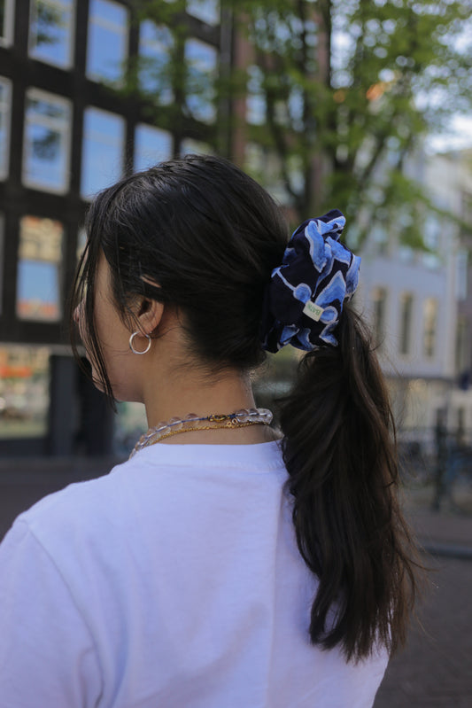 Person with a blue scrunchie batik mega mendung in their hair, standing outdoors.