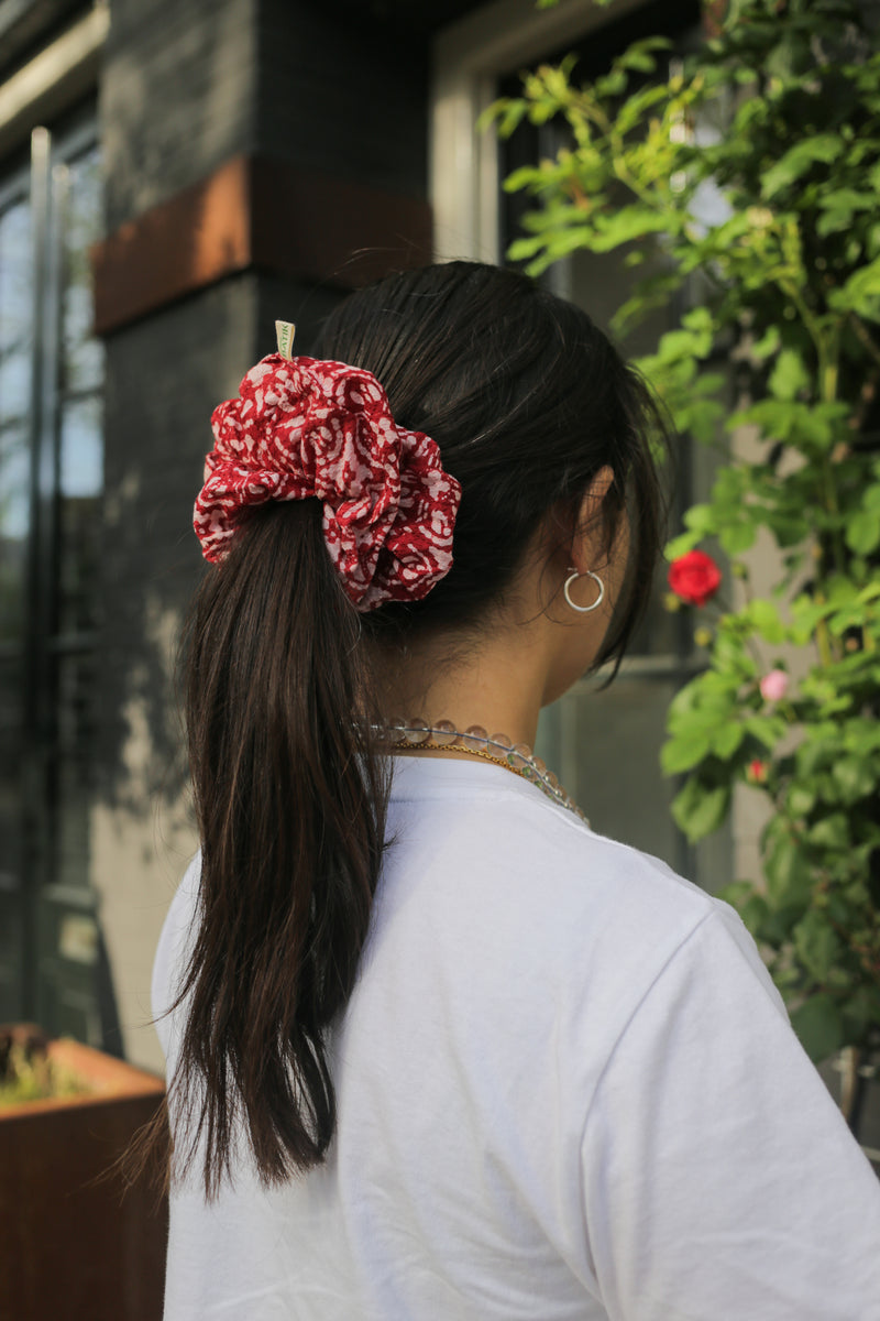 Person with a red and white scrunchie in their hair, standing outdoors with greenery. batik scrunchie titik