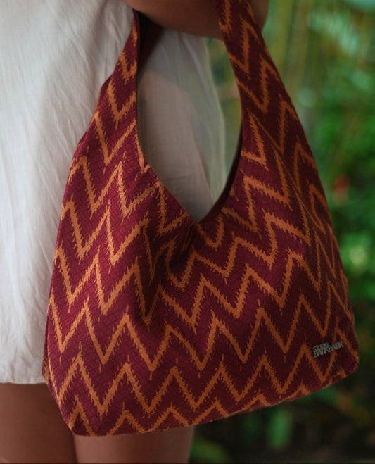 Person holding a red and yellow chevron Batik bag with a blurred green background